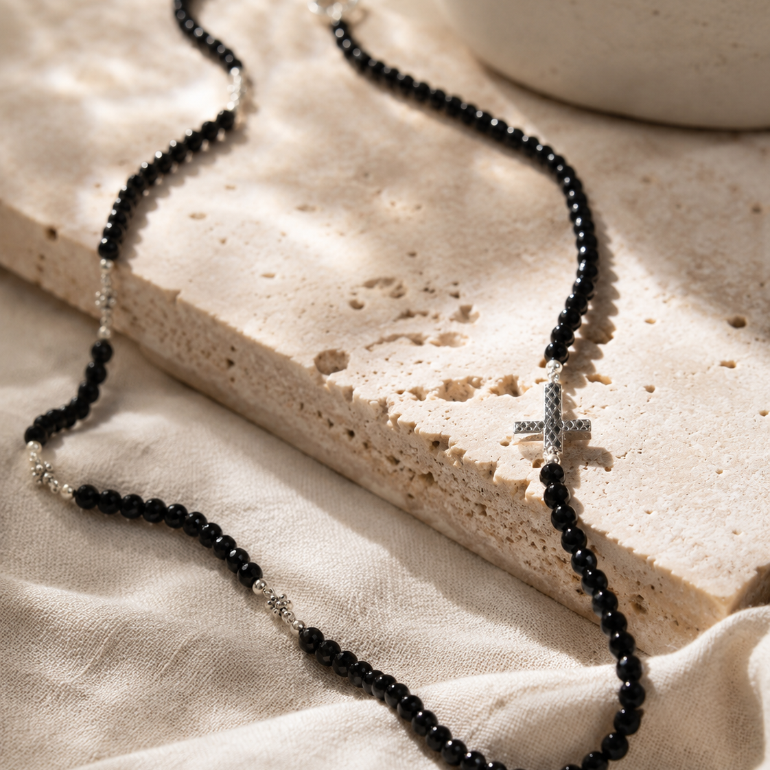 Close-up of polished black spinel beads and textured sterling silver cross accent in Black Spinel Sterling Silver Cross Necklace