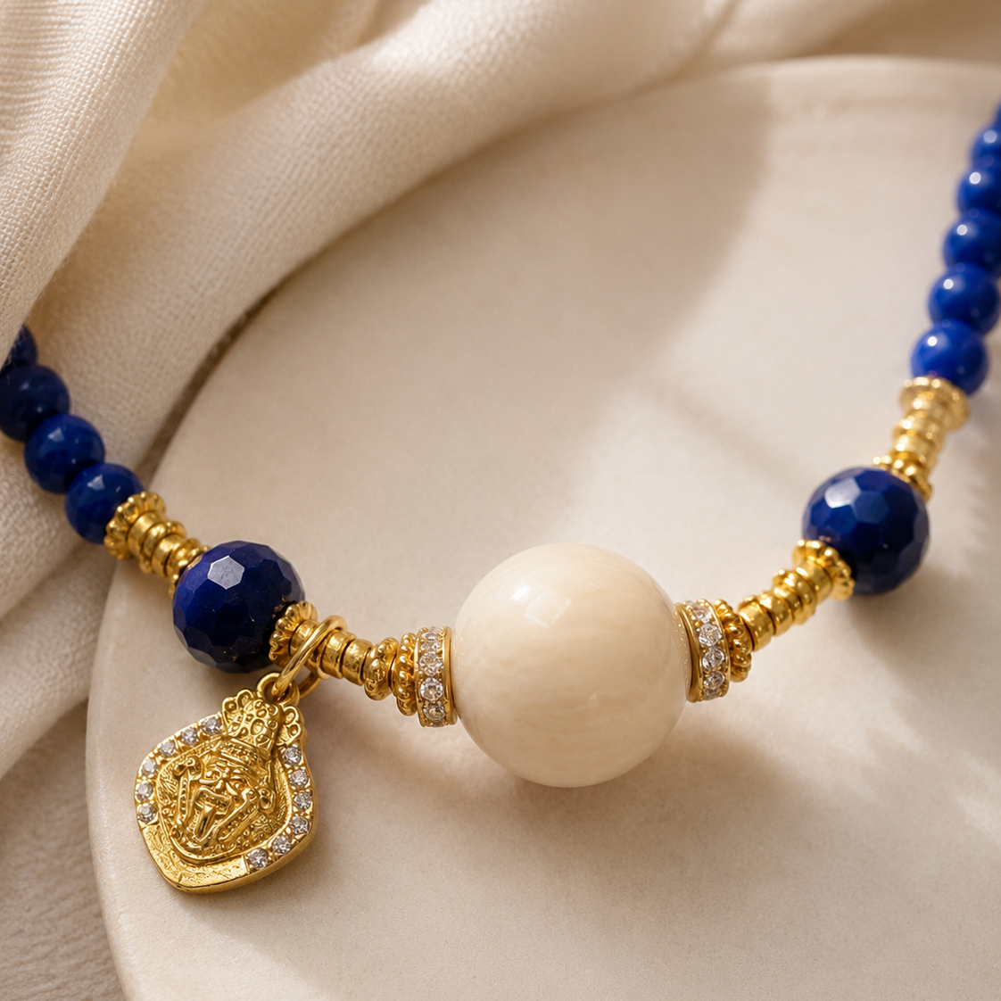 Close-up of lapis lazuli beads, cream resin focal bead, gold-plated sterling silver details, and charm in Lapis Lazuli Beaded Necklace