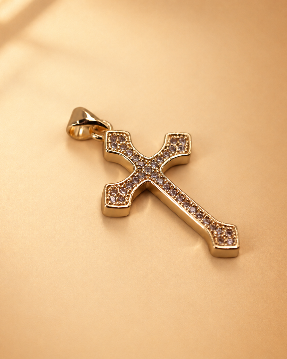 Low angled view of Clara cross pendant showing the polished gold-plated edge and clear accents across the front.