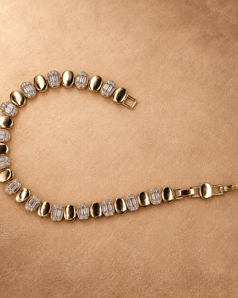 Dalia oval link bracelet laid in an open curve, showing the clasp, polished gold finish and clear rectangular accents.