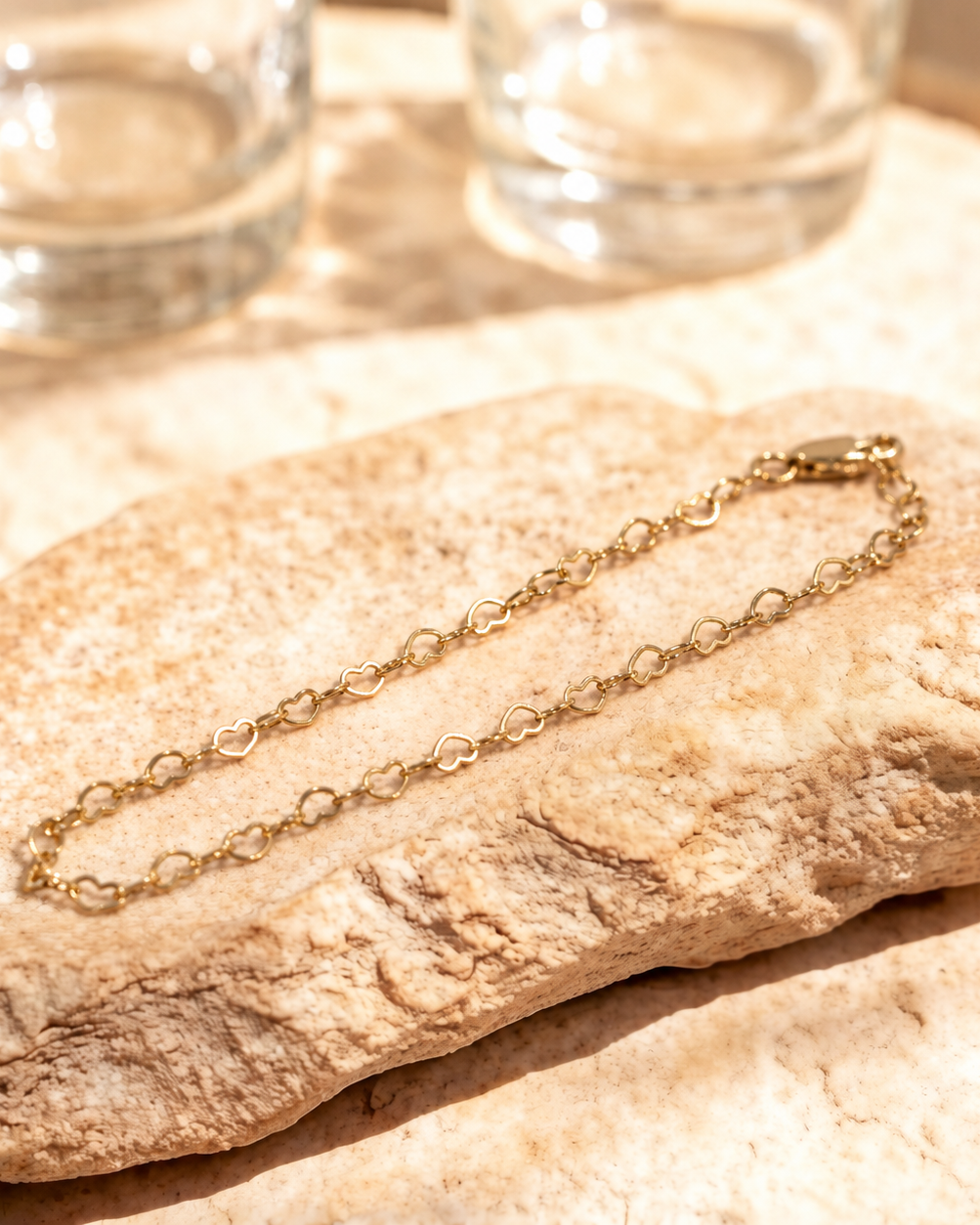 Angled view of Esme bracelet on a warm stone surface, showing the delicate open heart links joined by small oval links.