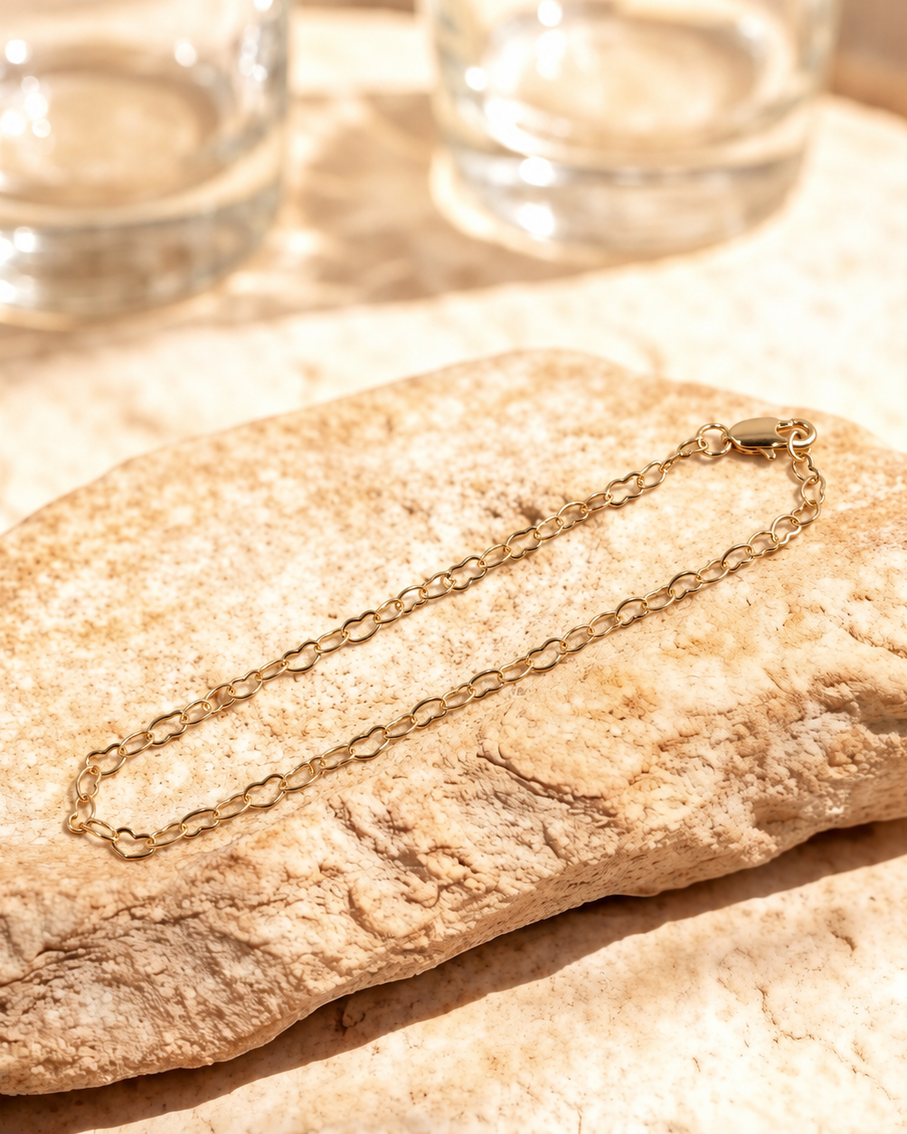 Full view of Esme 14K gold-plated heart link bracelet laid diagonally in a narrow oval on a textured stone surface.