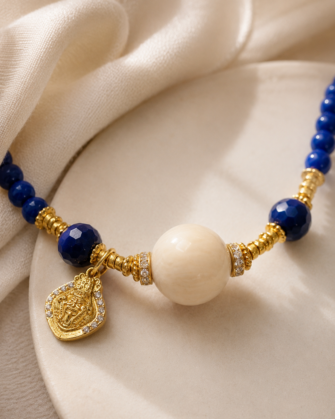 Close-up of lapis lazuli beads, cream resin focal bead, gold-plated sterling silver details, and charm in Lapis Lazuli Beaded Necklace