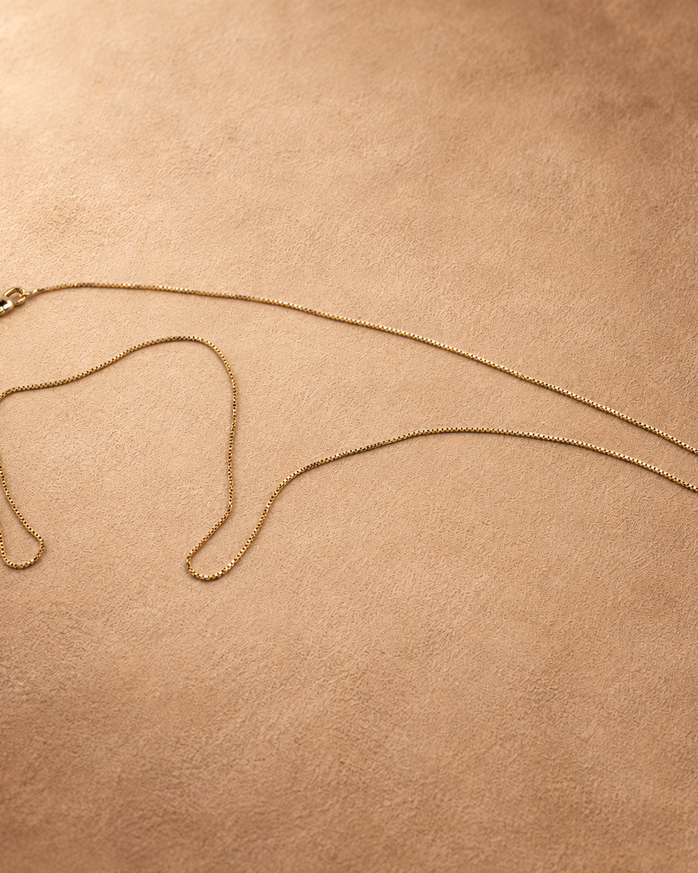 Angled full view of Linea gold-plated box chain necklace, showing its slender profile and small square links.