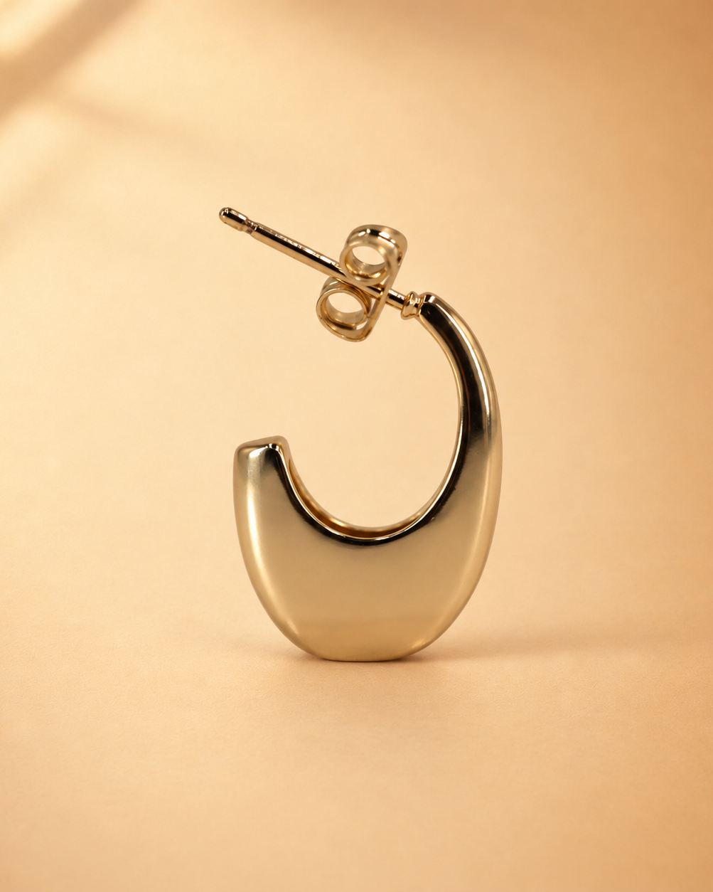 Lune 14K gold-plated steel earring standing upright, showing its polished crescent-shaped open hoop and butterfly backing.