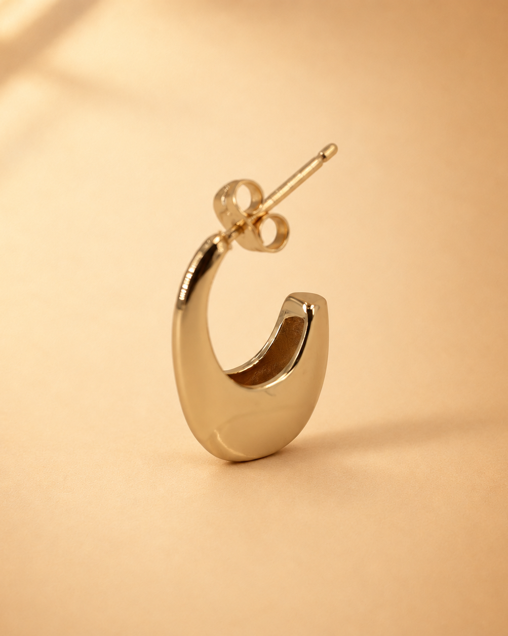 Angled view of Lune crescent hoop earring, showing its rounded lower curve, tapered upper edge and straight post.