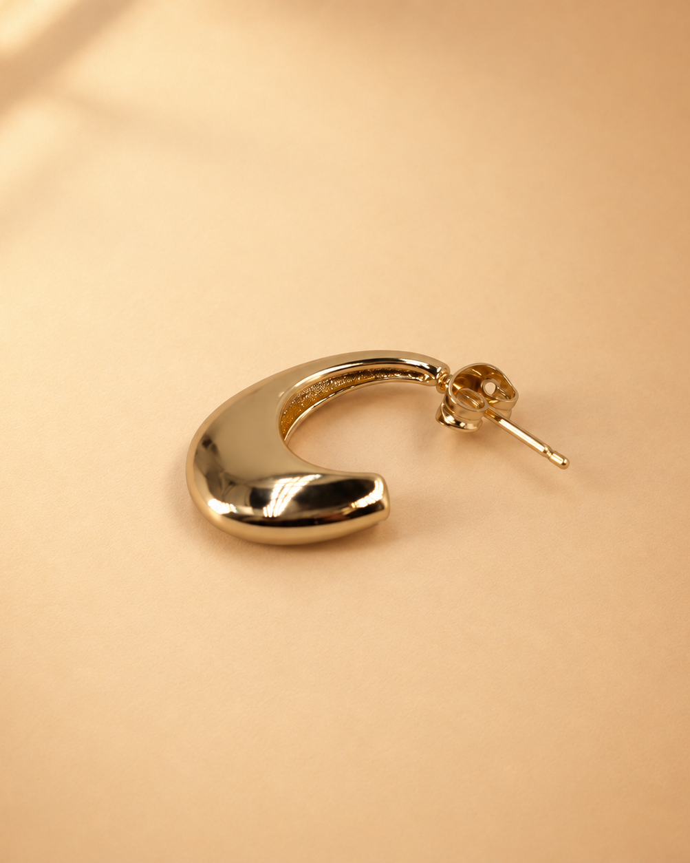 Lune gold-plated crescent hoop earring laid on its side, with the polished curved surface and post fastening visible.