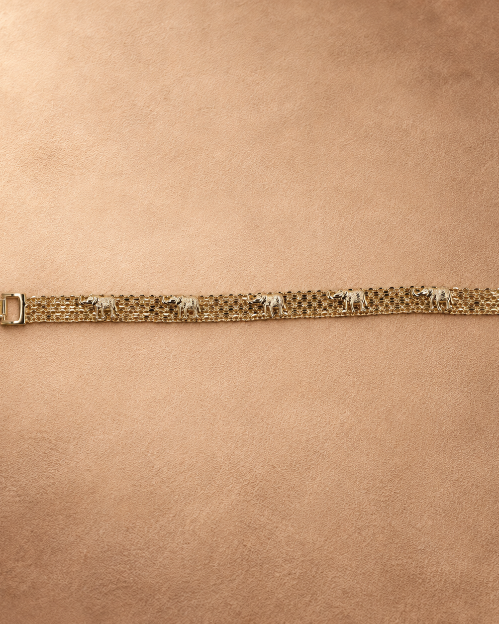 Full-length view of the Nila 14K gold-plated bracelet laid straight, with textured elephants along parallel chain rows and the clasp open.