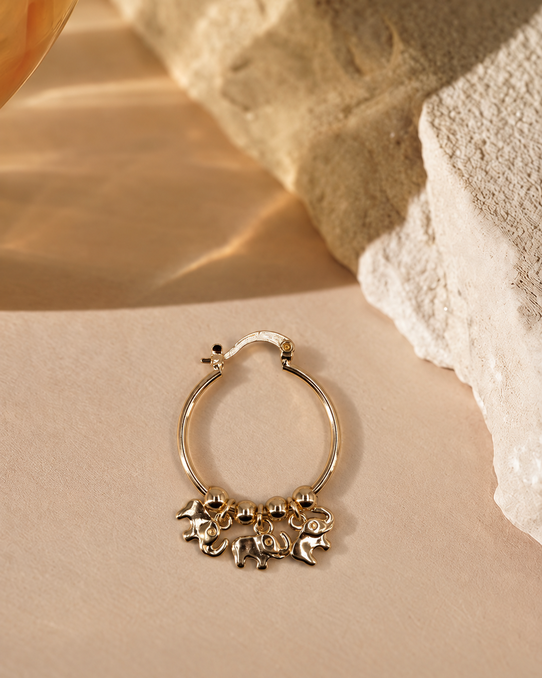Nila 14K gold-plated steel hoop earring with three dangling elephant charms and polished round beads along the bottom.