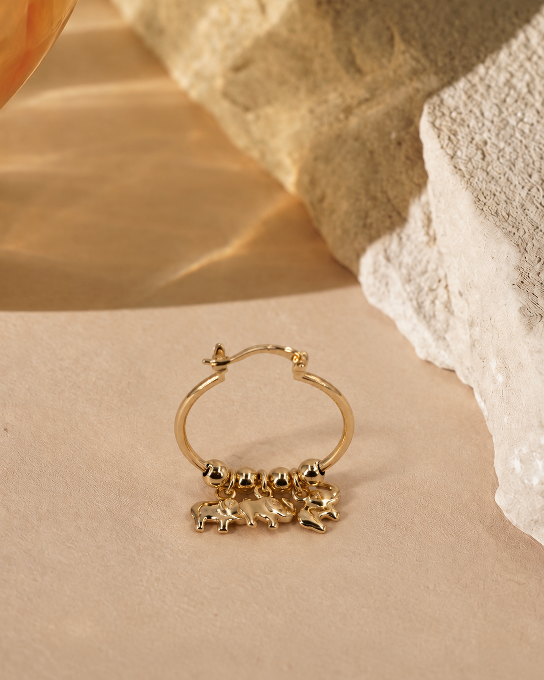 Nila gold-plated hoop earring at an alternate angle, showing the suspended elephant charms and hinged latch fastening.
