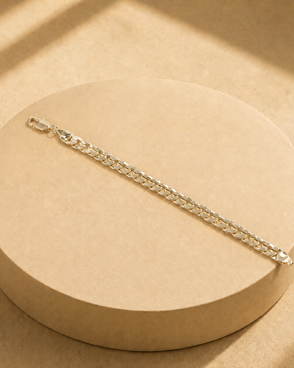Riva gold-plated curb chain bracelet laid straight across a round display, showing the full chain, clasp and polished end plates.