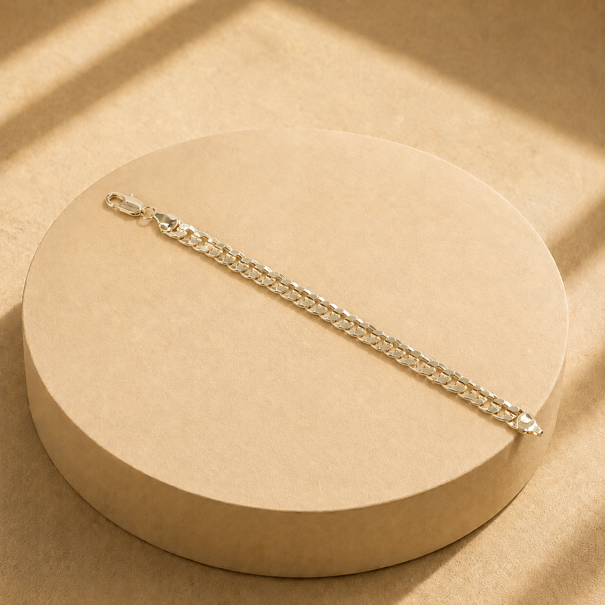 Riva gold-plated curb chain bracelet laid straight across a round display, showing the full chain, clasp and polished end plates.