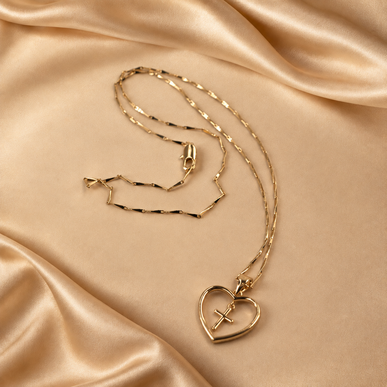 Amara 14K gold-plated necklace with an open-heart pendant and suspended cross, shown with its fine angular chain on champagne fabric.