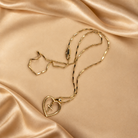 Angled view of the Amara 14K gold-plated heart-and-cross necklace, showing the pendant profile, fine chain and clasp on champagne fabric.