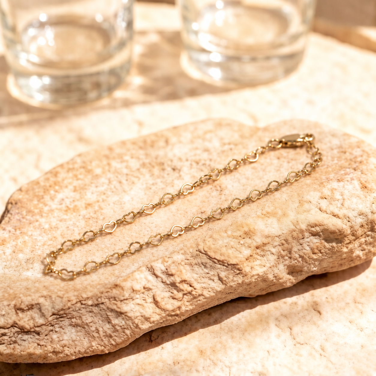 Angled view of Esme bracelet on a warm stone surface, showing the delicate open heart links joined by small oval links.