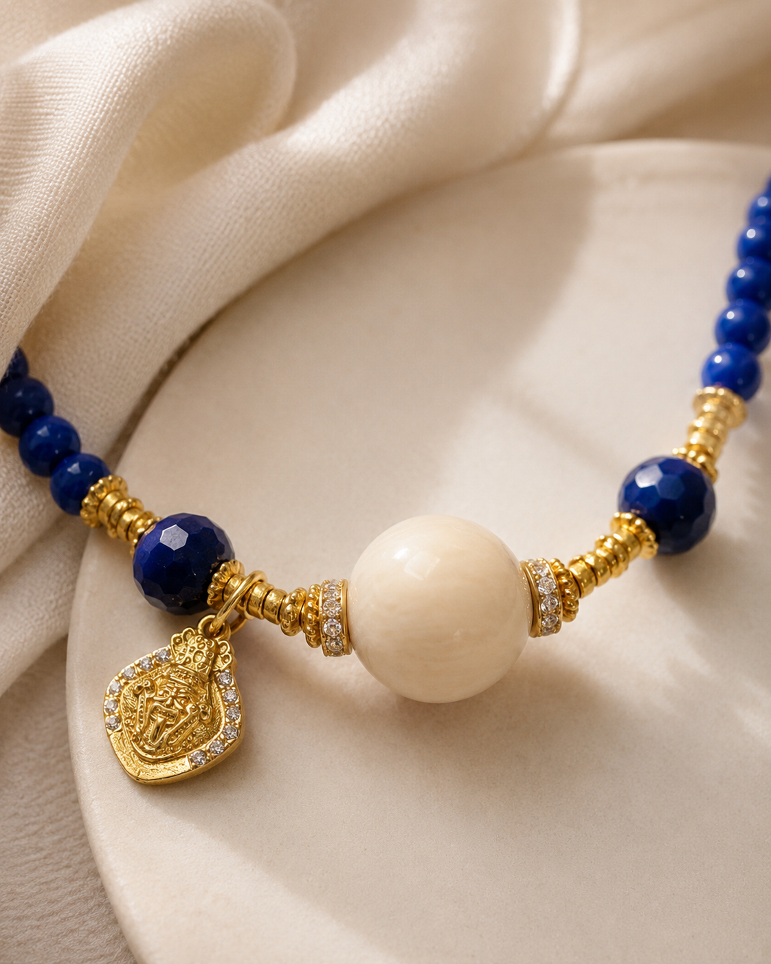 Close-up of lapis lazuli beads, cream resin focal bead, gold-plated sterling silver details, and charm in Lapis Lazuli Beaded Necklace