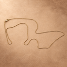 Linea box chain necklace arranged in loose curves on a warm textured surface, with the clasp at the upper left.