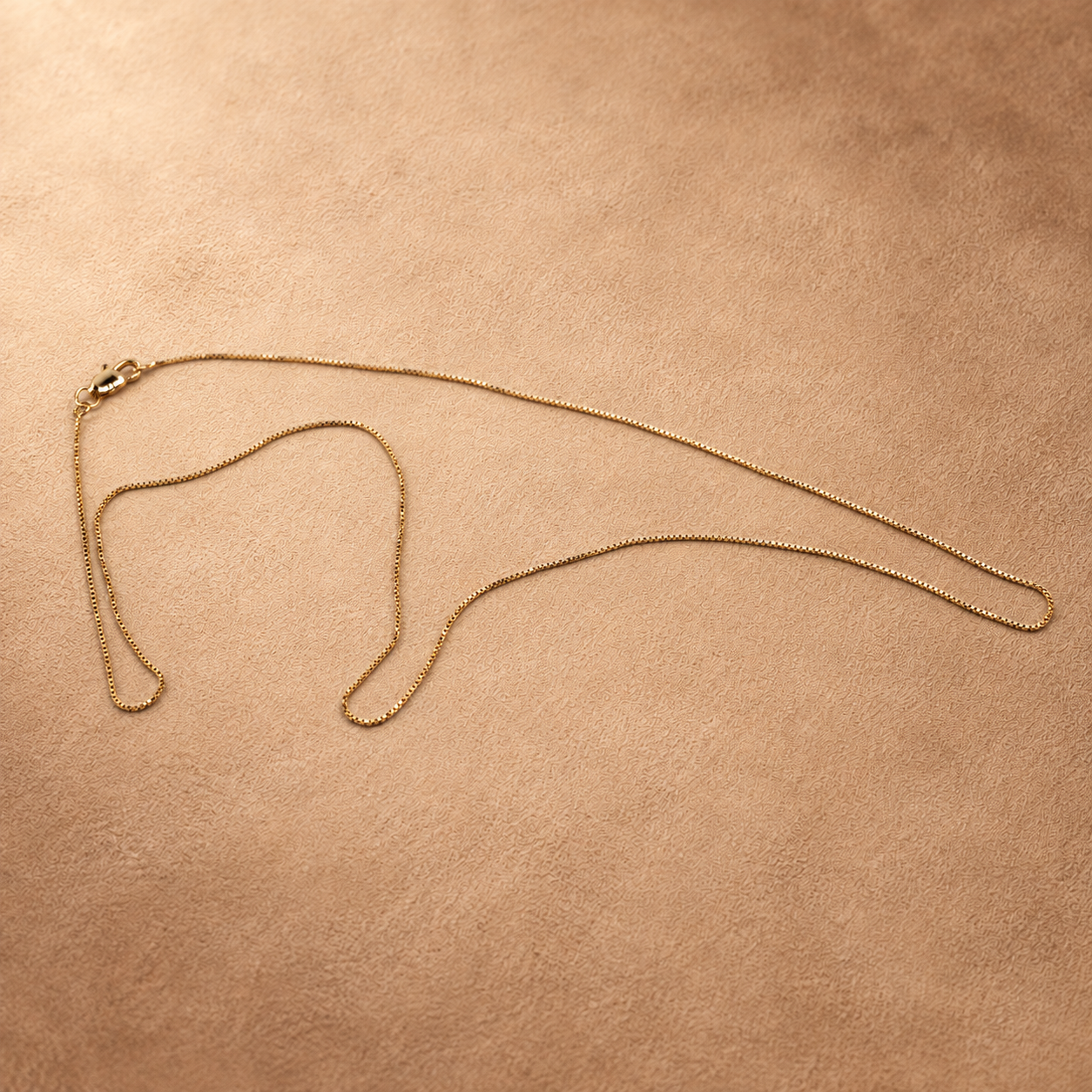 Angled full view of Linea gold-plated box chain necklace, showing its slender profile and small square links.