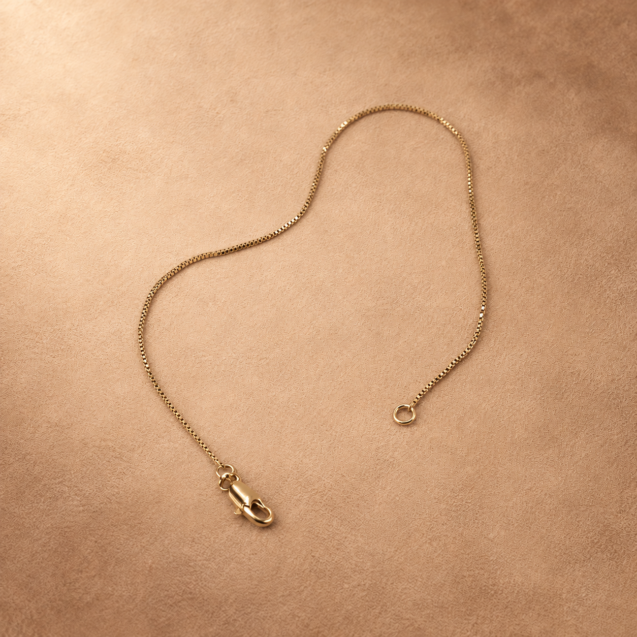 Linea fine chain bracelet laid open, with the lobster clasp and end ring separated on a warm textured background.