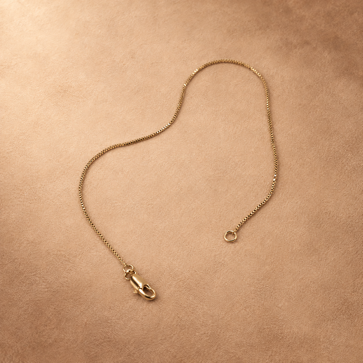 Linea fine chain bracelet laid open, with the lobster clasp and end ring separated on a warm textured background.