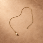 Linea fine chain bracelet laid open, with the lobster clasp and end ring separated on a warm textured background.