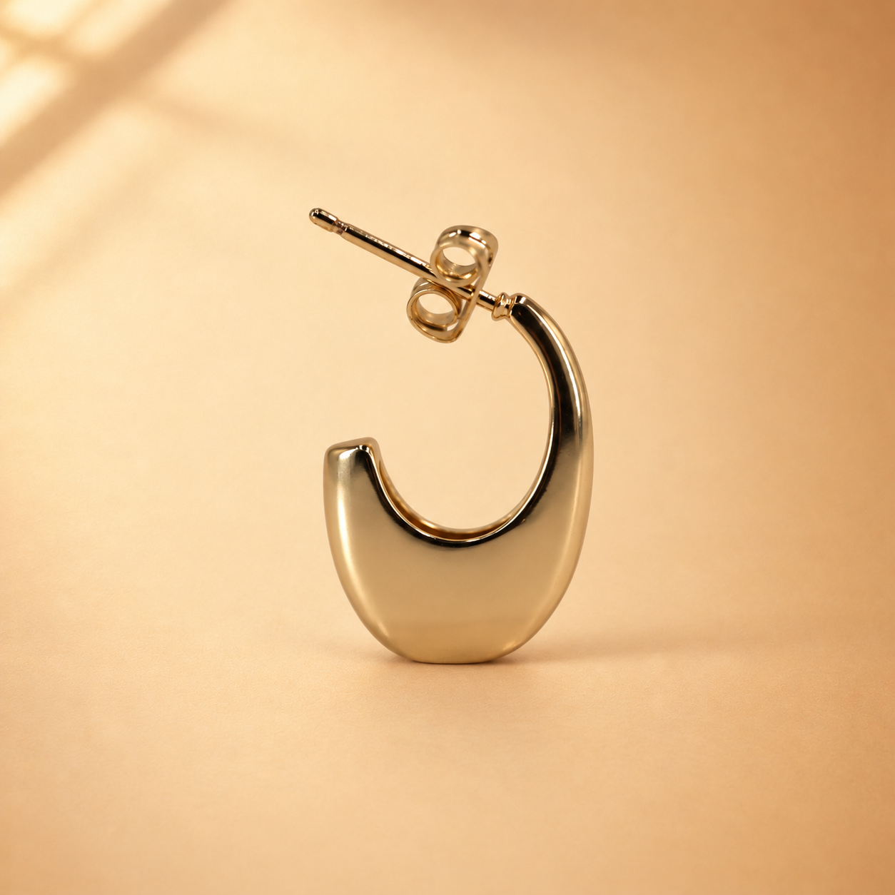 Lune 14K gold-plated steel earring standing upright, showing its polished crescent-shaped open hoop and butterfly backing.