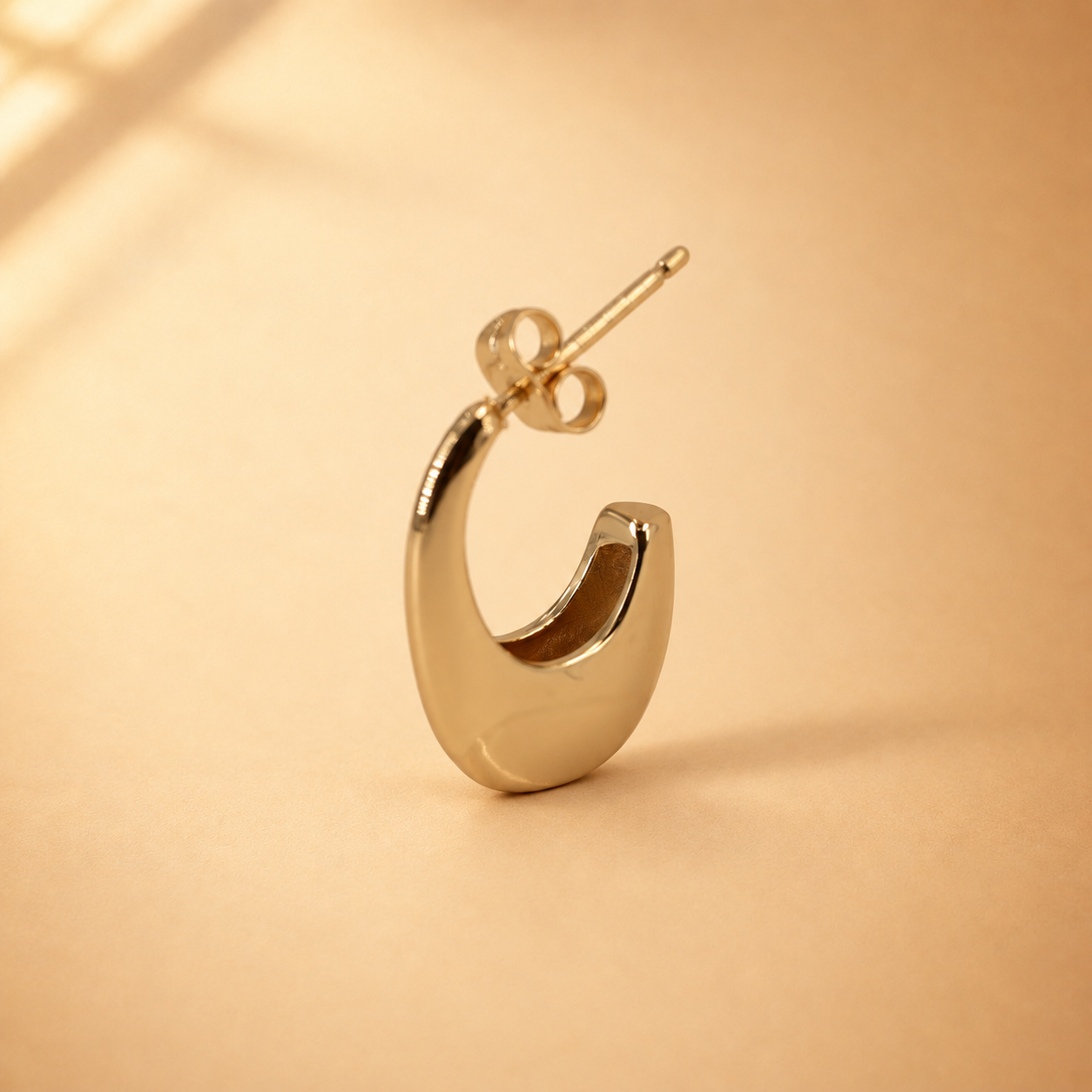 Angled view of Lune crescent hoop earring, showing its rounded lower curve, tapered upper edge and straight post.