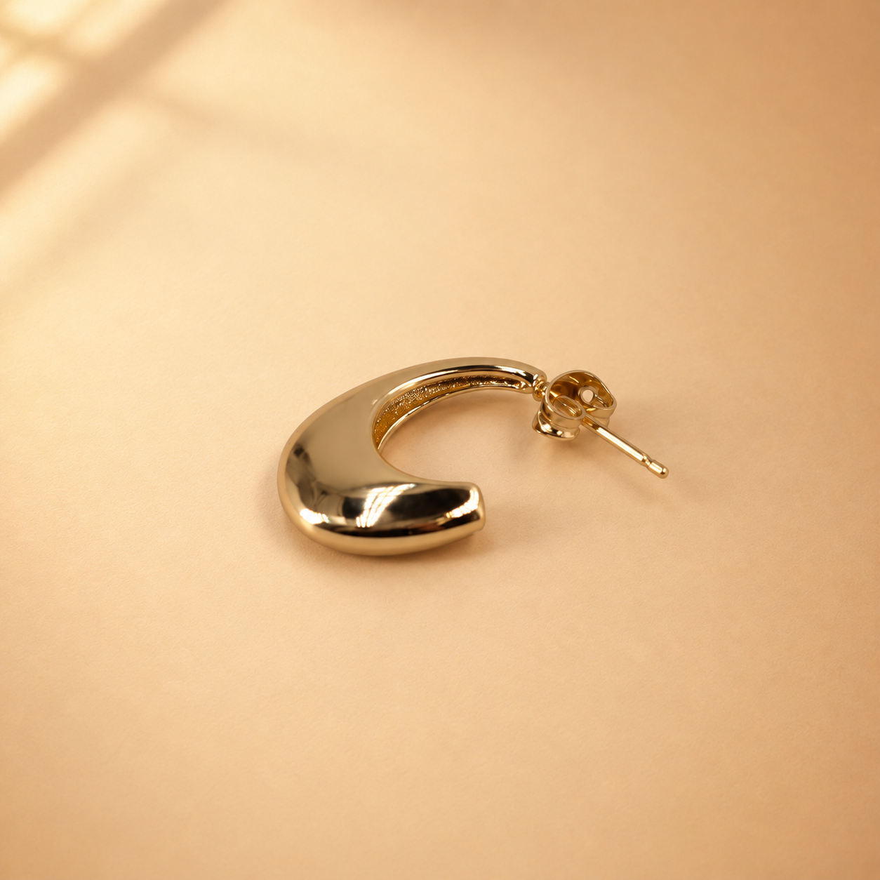 Lune gold-plated crescent hoop earring laid on its side, with the polished curved surface and post fastening visible.