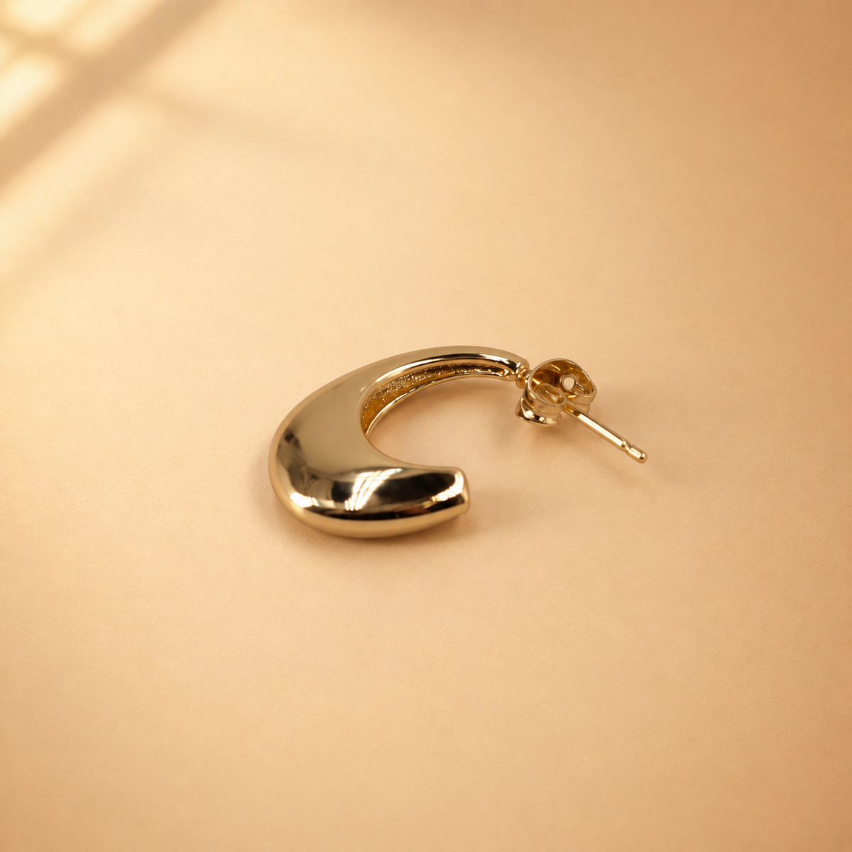 Lune gold-plated crescent hoop earring laid on its side, with the polished curved surface and post fastening visible.