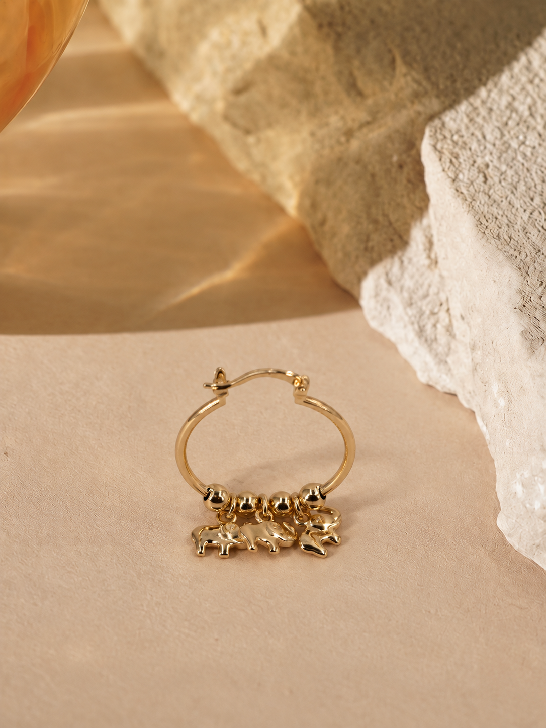 Nila gold-plated hoop earring at an alternate angle, showing the suspended elephant charms and hinged latch fastening.